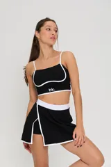 Conjunto deportivo de dos piezas compuesto por un top de tirantes finos con detalle de ribete blanco y logo estampado, y una pollera short con cintura elástica blanca y tajo lateral con ribete blanco.
