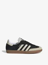 Zapatillas Adidas Samba OG, color negro con las tres tiras laterales en blanco y suela de goma marrón.