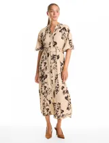 Vestido maxi de crepe color beige con estampado floral en tonos marrones y negros. Presenta cuello a la base, escote en V, abertura central con botones y cintura con lazo de ajuste y hebilla.