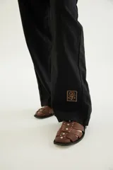 Pantalón de corte recto y tiro medio con costuras a la vista, bolsillos delanteros y traseros, y un detalle de pin de la marca en el ruedo.