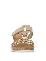 Sandalias de plataforma baja con diseño de tiras cruzadas en color beige y dorado. Presentan una tira superior con cierre de velcro y una tira frontal con detalle de calados geométricos y pequeñas tachas metálicas. La plantilla es acolchada y la suela tiene textura tipo yute.