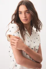 Pijama de algodón color blanco con pequeño estampado floral azul, compuesto por una camisa de mangas cortas con cuello solapa, botones frontales y bolsillo en el pecho, y un short con elástico y lazo ajustable en la cintura.