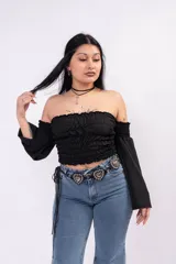 Remera negra con cuerpo fruncido en nido de abeja, diseño off-shoulder y mangas largas fluidas.