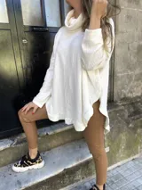 Sweater color beige de tejido de punto con cuello alto, mangas largas y corte asimétrico con volados en el ruedo.