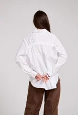 Camisa de algodón blanca con bordados florales en color bordó a lo largo de la botonadura frontal y en el cuello. Presenta mangas largas con puños abotonados y un corte holgado.