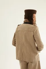 Chaqueta corta de inspiración motoquera color beige, confeccionada en lino fantasía, sin forro, con cierres decorativos, broches de presión y bolsillos delanteros funcionales. Presenta detalle bajo el cuello y en vueltas de mangas en color mostaza y rayas.