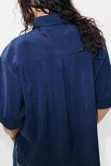 Camisa de cuello solapa y manga corta con dobladillo, presenta bolsillos de plastrón en el frente, bajo asimétrico y cierre frontal con botones ocultos.