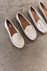 Mocasines de cuero color dorado con acabado texturizado, diseño clásico de punta redondeada y costuras visibles en el empeine. Cuentan con suela plana y flexible.