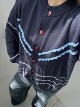 Saco de punto color crema con detalles en crochet verde, cierre frontal con botones y mangas largas.