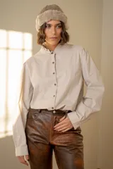Camisa de algodón color beige con cuello mao y detalle de volado, cierre frontal con botones y mangas largas con puños.