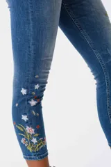 Jeans de corte ajustado y tiro medio en color azul, con detalles de bordados florales coloridos en una de las piernas.