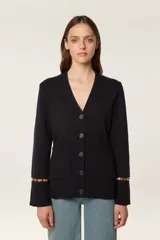 Cárdigan de punto color azul marino, con escote en V, cierre frontal con botones al tono y bolsillos de parche. Presenta mangas largas con aberturas decoradas con cuentas doradas en los puños.