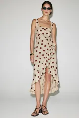 Vestido midi de mezcla de lino y viscosa en color beige con estampado de lunares bordó. Cuenta con escote recto, tirantes anchos y un volante lateral en cascada que recorre el frente hasta el bajo asimétrico.