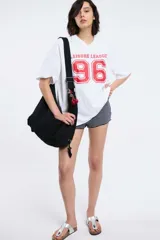 Remera oversize gris oscuro con cuello en V y mangas cortas. Presenta una estampa frontal estilo universitario con el número "09" y las inscripciones "MVD", "UY" y "PIMENTÓN ACTIVE" en tonos celestes y blancos.