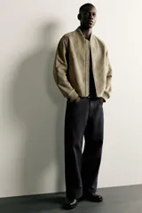 Campera bomber color verde militar de corte relaxed fit, confeccionada en tejido efecto ante, con cuello, puños y dobladillo en rib elástico, bolsillos frontales de vivo y cierre central con cremallera.