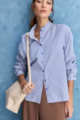 Camisa de rayas blancas y azules con cuello mao decorado con volados sutiles, cierre frontal de botones y mangas largas.