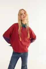 Remera de manga larga con corte boxy, confeccionada en algodón. Presenta un diseño de rayas horizontales en tonos azul y fucsia, con detalles de rayas verticales en los codos, tajos laterales y logo bordado en el pecho.