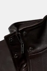 Chaqueta tipo bomber de piel con cuello alto, manga larga con hombreras y puños elásticos. Presenta bolsillos delanteros, bajo elástico y cierre frontal con cremallera y botones ocultos por solapa.
