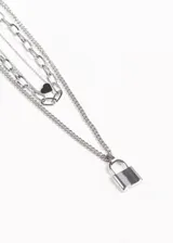 Collar de acero quirúrgico plateado con tres cadenas de diferentes largos y estilos. La cadena más corta tiene un dije de corazón negro, la más larga tiene un dije de candado plateado.