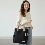 Cartera tipo shopper color beige con bolsillos laterales y un bolsillo frontal con tirador de cordón trenzado. Cuenta con asas superiores de lona.