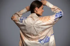 Camisa de batista blanca de corte oversize, con diseño estampado de tigres y flores en tonos azul y naranja. Presenta cuello camisero, mangas largas con puños anchos, espalda con tabla y ruedo irregular.