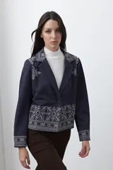Blazer de gamuza color terracota con bordados decorativos en color crudo en solapas, puños y ruedo. Presenta corte recto, solapas clásicas y cierre frontal con un botón forrado.