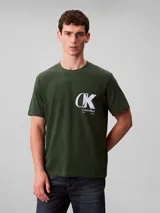 Remera de cuello redondo y manga corta, confeccionada en tejido de punto de algodón. Presenta un estampado frontal con el monograma de Calvin Klein y el logo de la marca en color blanco sobre un fondo verde oscuro.