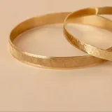 Esclava rígida de oro 18k con acabado satinado y diseño de cinta plana. Presenta una textura fina y elegante en toda su superficie.