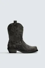 Bota estilo cowboy fabricada en tejido denim de algodón con efecto lavado, diseño de caña media con tiradores laterales, horma cuadrada y tacón ancho.