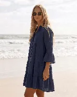 Vestido corto de lino natural color gris, con diseño amplio de capas, escote en V con botones frontales y mangas largas con volados en los puños.