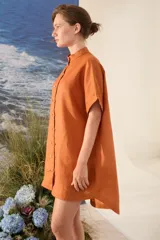 Vestido corto color beige de lino, con moldería amplia, manga corta, cuello mao y cierre frontal con botones dorados.