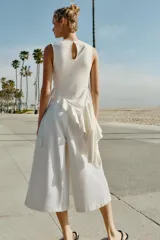 Top de algodón color crudo, con diseño sin mangas, cuello redondo y bajo asimétrico acabado en volante. Presenta frunces diagonales con detalles de cordones y cierre trasero con abertura y botón.