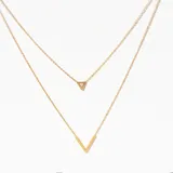 Collar doble dorado con cadena fina. El collar superior tiene un dije de triángulo con un cristal incrustado, mientras que el collar inferior tiene un dije en forma de V.