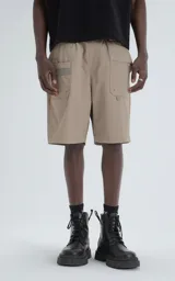 Bermuda estilo técnico color beige, confeccionada en microfibra liviana. Presenta cintura elástica con cinturón integrado de cinta negra con hebilla de plástico. Cuenta con múltiples bolsillos cargo, incluyendo uno lateral con panel de malla.