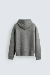 Chaqueta de punto con capucha, corte relajado, manga larga, bolsillos laterales y cierre frontal con cremallera. Presenta acabados en rib en puños y bajo.