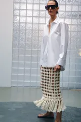 Falda midi de punto crochet en color crudo, con diseño de red, cintura elástica y bajo terminado en flecos largos.