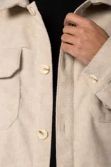 Campera corta tipo sobrecamisa de paño elastizado color beige, con cuello camisero, cierre frontal con botones veteados y dos bolsillos frontales con tapa.