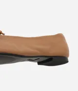 Zapatilla tipo bailarina Satinato confeccionada en cuero color tostado, con punta redondeada y detalle de mini lazo en la parte superior. Cuenta con suela plana de baja altura.