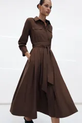 Vestido midi de estilo camisero color verde oscuro, con cuello solapa, escote en pico y cierre frontal con botones. Presenta manga larga, bolsillos laterales ocultos, solapas decorativas en el pecho y cinturón de lazada en el mismo tejido.