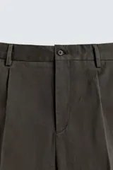 Pantalón relaxed fit de traje color marrón oscuro, confeccionado en tejido con mezcla de algodón. Cuenta con bolsillos frontales, bolsillos traseros de doble vivo con botón y efecto lavado. Cierre frontal con cremallera y botón.