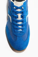 Calzado deportivo de color azul con detalles en blanco y suela de goma con diseño. Cuenta con collarín acolchado, lengüeta y cordones.