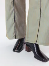 Bota de caña media con punta cuadrada, confeccionada en color negro. Presenta una costura central con bordado en color contrastante y un taco bloque de madera de 6 cm. Cuenta con cierre en la parte posterior.