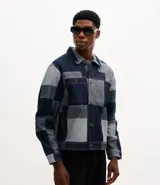 Campera de jacquard de algodón con diseño patchwork de cuadros en tonos azules. Presenta cuello inglés, cierre frontal con botones metálicos, mangas largas y bolsillos delanteros.