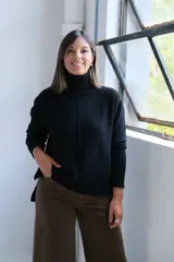 Polerón negro de cuello alto, con diseño de costura vertical central y puños acanalados. Presenta un corte holgado con dobladillo asimétrico, siendo más largo en la parte posterior.