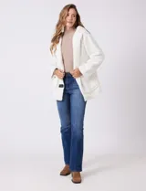 Campera tipo teddy de textura suave y esponjosa en color blanco, con cierre frontal mediante botones y detalles de apliques en cuero sintético negro en la solapa. Presenta bolsillos frontales y un diseño cómodo y abrigado.
