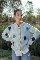 Cardigan de lana color celeste con cuello redondo, cierre frontal con botones color naranja y flores bordadas en azul y celeste.