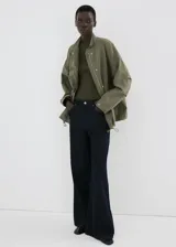 Chaqueta estilo militar verde militar, de diseño oversize, cuello alto, cierre frontal con cremallera y botones ocultos bajo tapeta, bolsillos con solapa y bolsillos de ribete en el pecho.