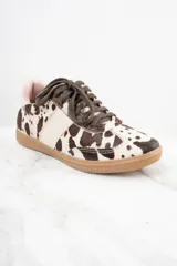Zapatillas bajas con estampado de vaca en tonos marrón y blanco, con cordones marrones y suela de goma color caramelo.