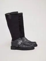 Bota híbrida de caña alta confeccionada en lona negra en la parte superior y cuero negro en la base tipo mocasín, con plataforma, suela track y tira con hebilla metálica cruzada en el empeine.