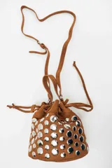 Cartera tipo bucket bag de gamuza negra, decorada con múltiples tachas metálicas plateadas de forma circular. Cuenta con cierre de cordón ajustable y asa superior.